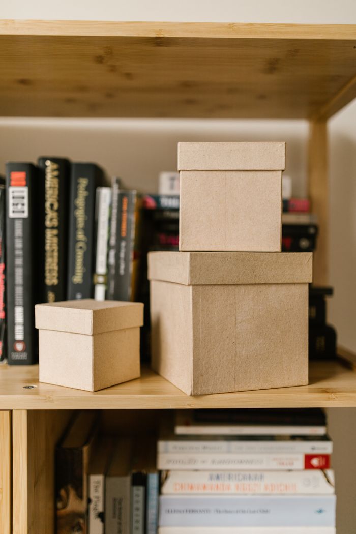 mobile-01 Close-up of cardboard boxes on a wooden bookshelf surrounded by various books.
